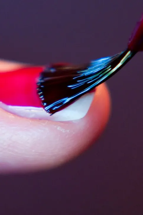 Pincel cargado de esmalte rojo pintando una uña, primer plano