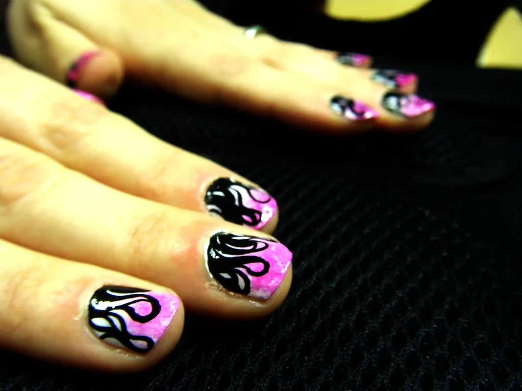 Uñas cortas fucsia con flames negras estilo Y2K sobre fondo negro
