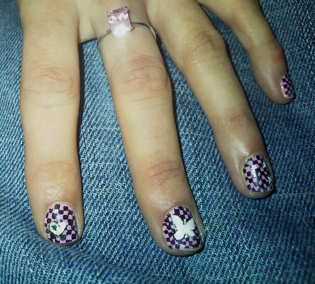 Uñas con damero violeta y blanco, una mariposa pintada y un anillo