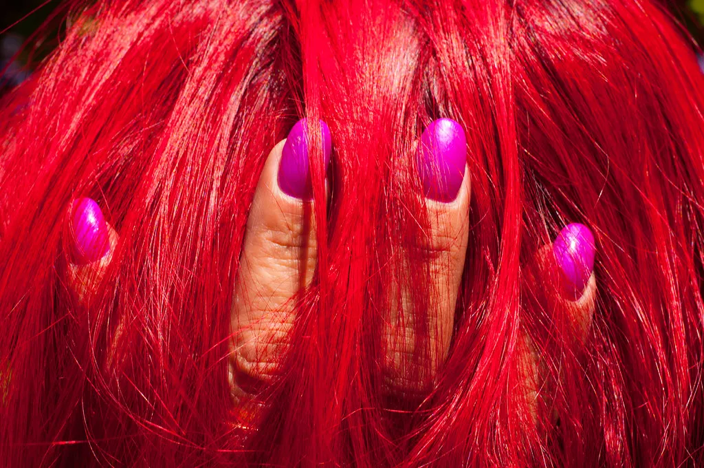 Uñas esculpidas fucsia contra una melena teñida de rojo fuego