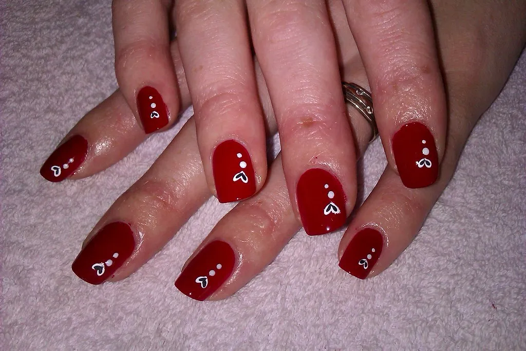 Uñas rojas con corazones blancos pintados a mano alzada