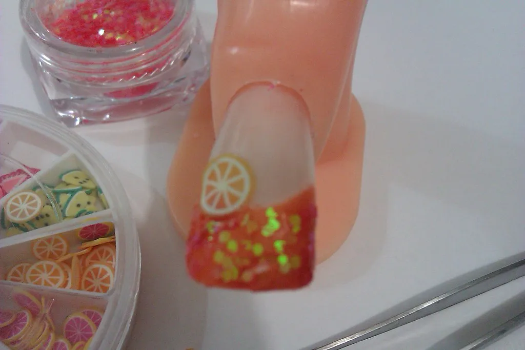 Uña con frutitas encapsuladas junto a potes de glitter